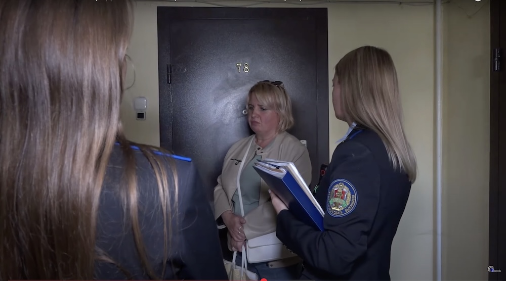 Владелица квартиры пинчанка Оксана (посередине) и судебные приставы около двери в захламленную мусором квартиру в Пинске. Скриншот с сюжета ТРК «Пинск».