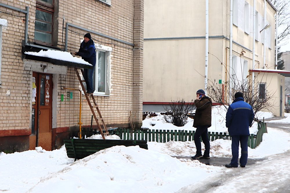 Коммунальщик чистит от снега козырек подъезда, который потом рухнет. Фото: Kraj.by